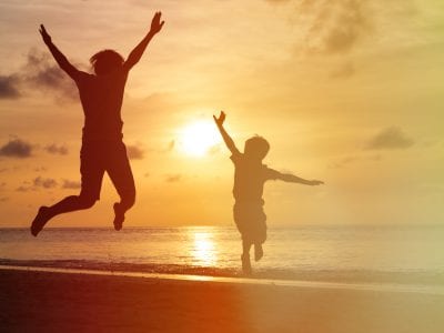 father and son jumping at sunset beach